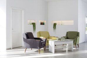 A modern living room with a white door, three chairs, a white coffee table, and wall-mounted shelves with decorative items. - El Guarapo Apartamentos (Teguise)