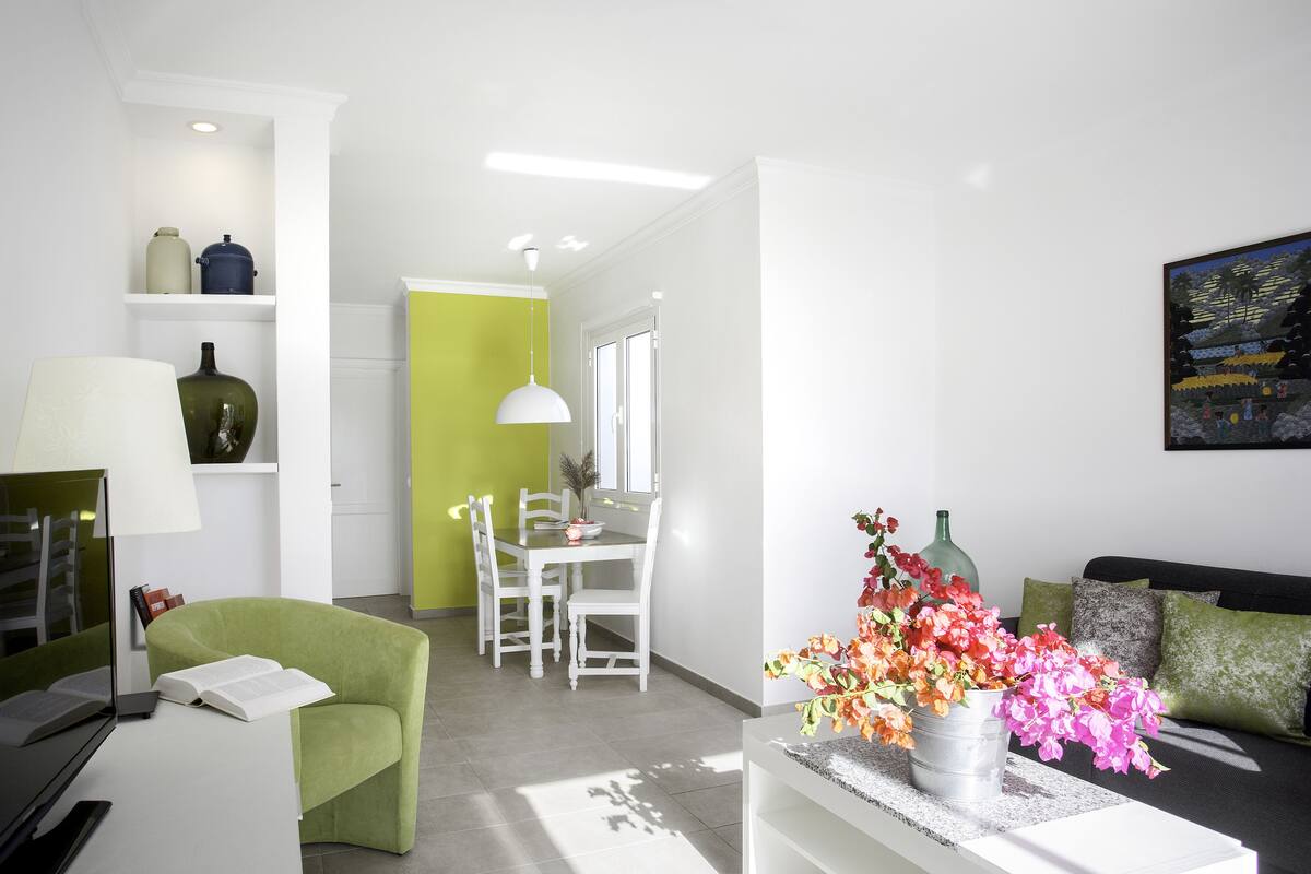 A modern living room with a green armchair, a white sofa, and a dining area with a table and chairs.