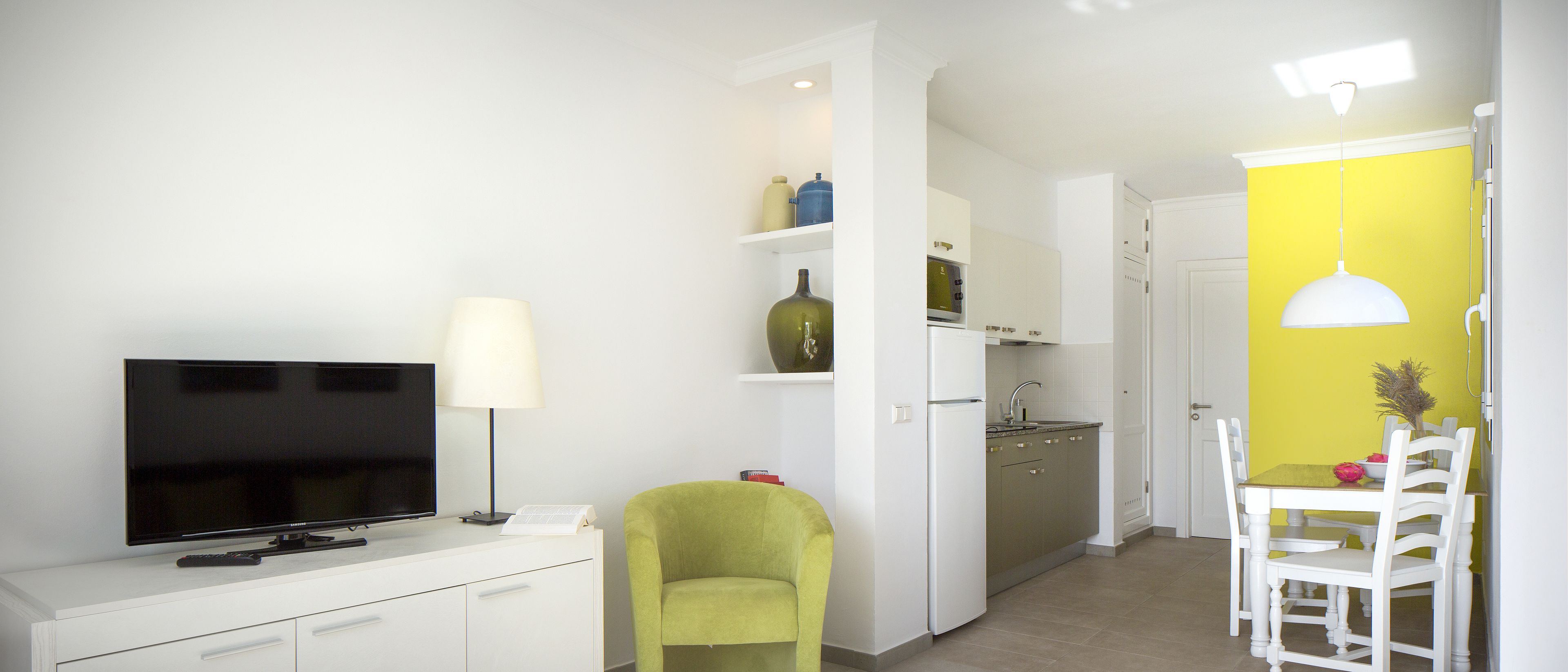 Un salon moderne avec un téléviseur à écran plat, une lampe, un fauteuil vert et un coin repas avec un mur jaune.