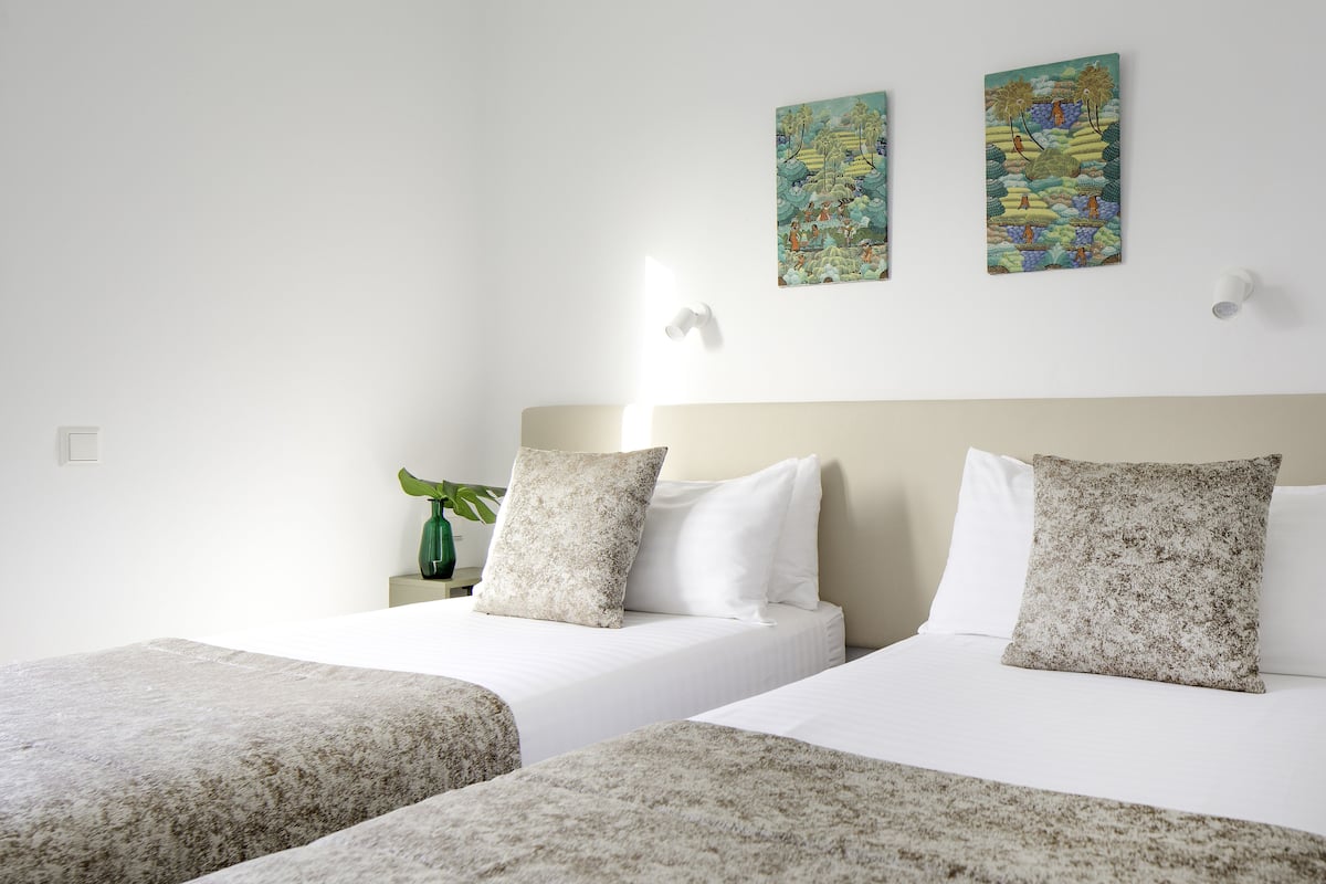 A hotel room with two beds, white bedding, and two wall-mounted artworks.