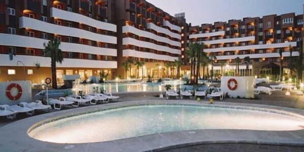 A hotel with a swimming pool, multiple balconies, and a well-lit exterior.