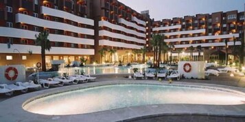 Un hotel con piscina, varios balcones y fachada bien iluminada.