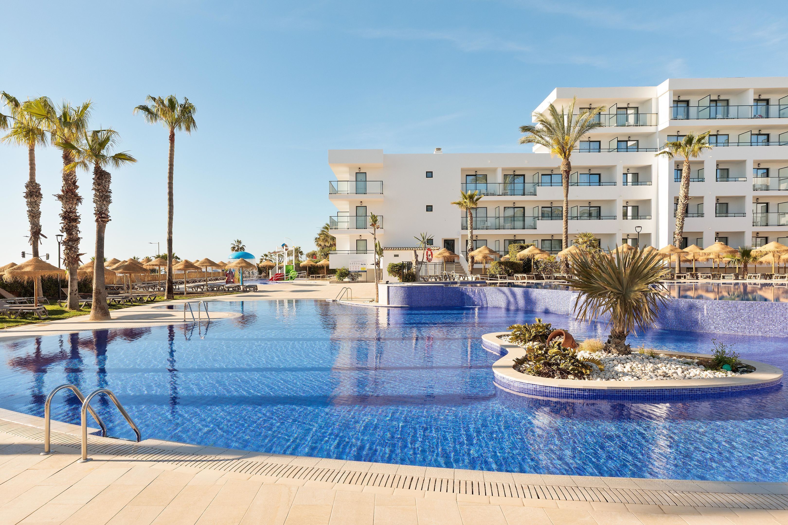 A swimming pool with a palm tree and a modern hotel building in the background.