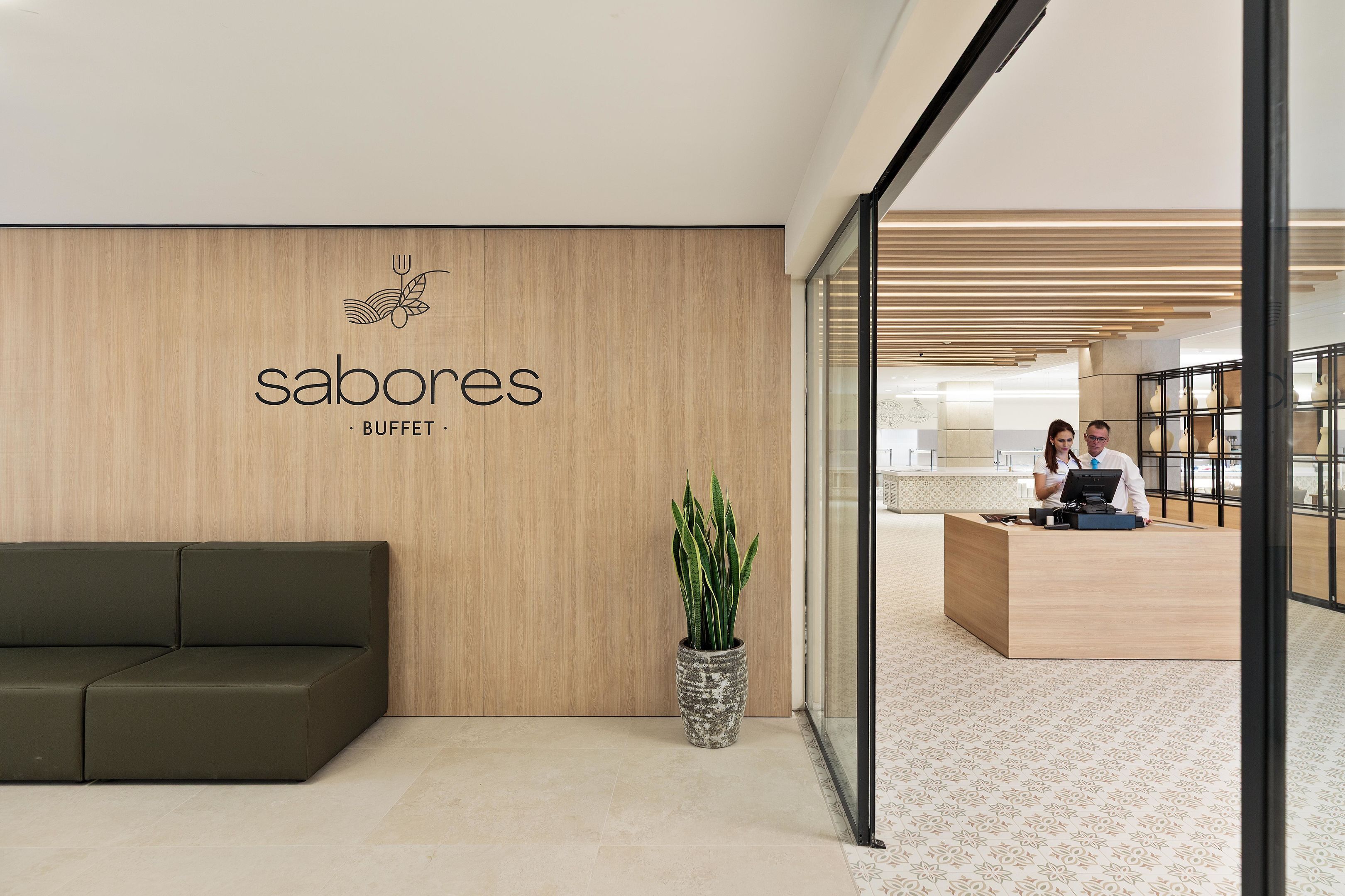 Una moderna zona de recepción con un muro de madera, un mostrador de recepción, un sofá verde y una planta en maceta.