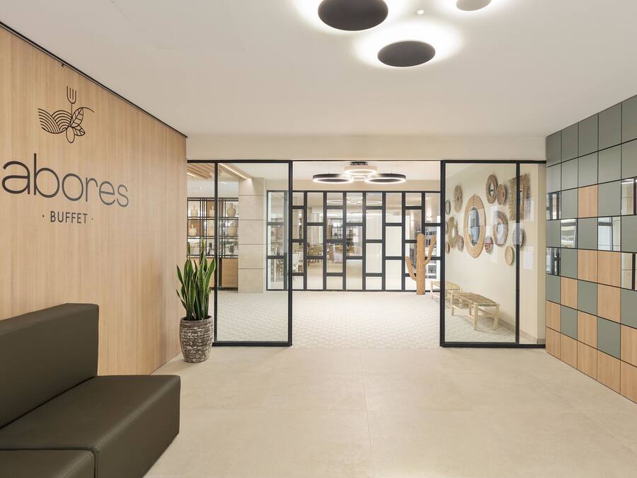 A modern lobby with a reception desk, a potted plant, and a buffet area in the background.