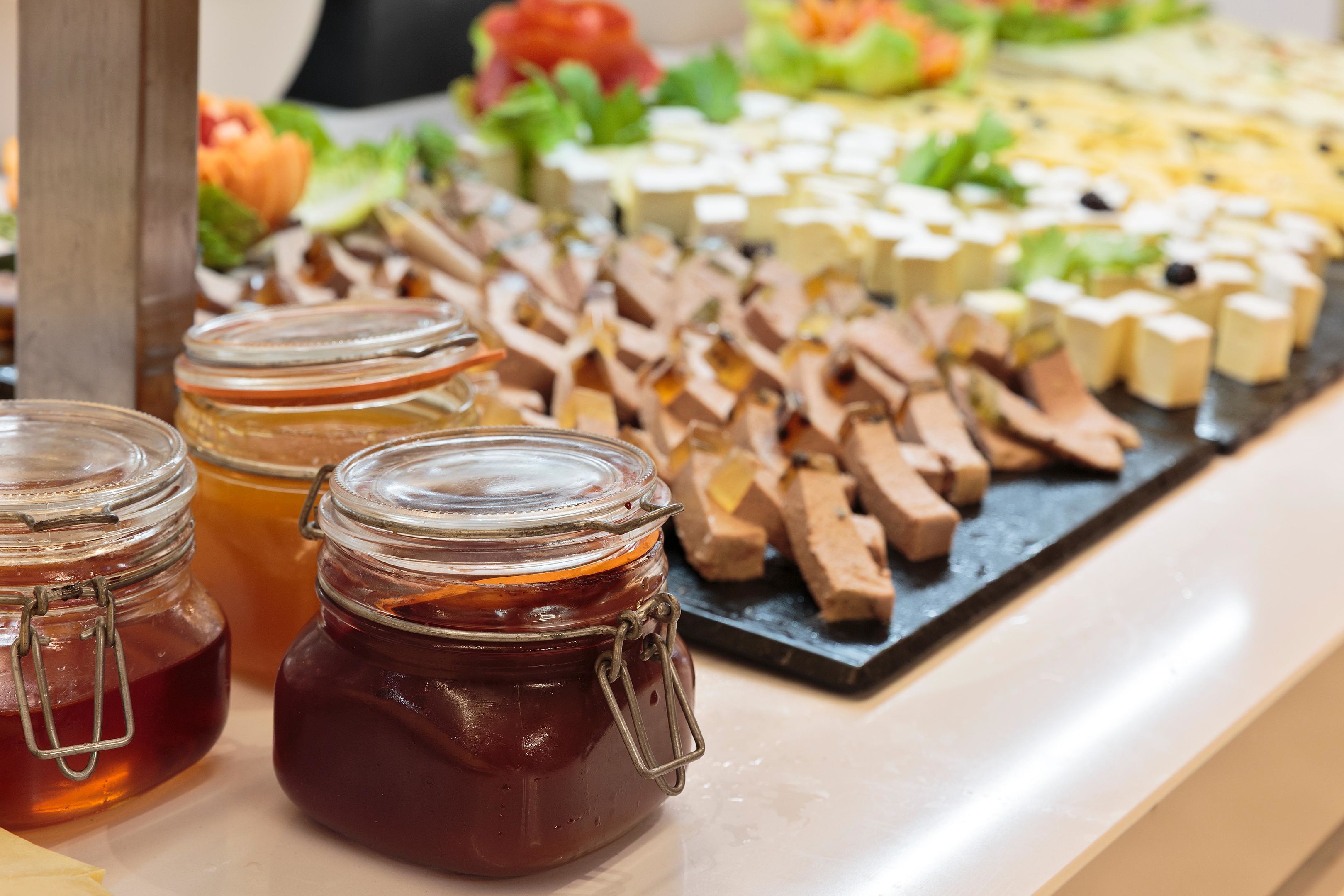 A buffet table with various food items and jars of honey.