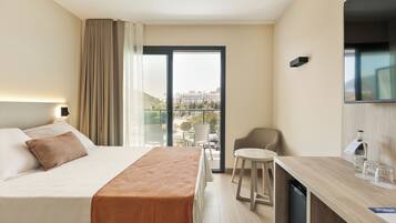 Habitación de hotel con cama, un rincón de comedor, una silla, televisión y vista a la ciudad.
