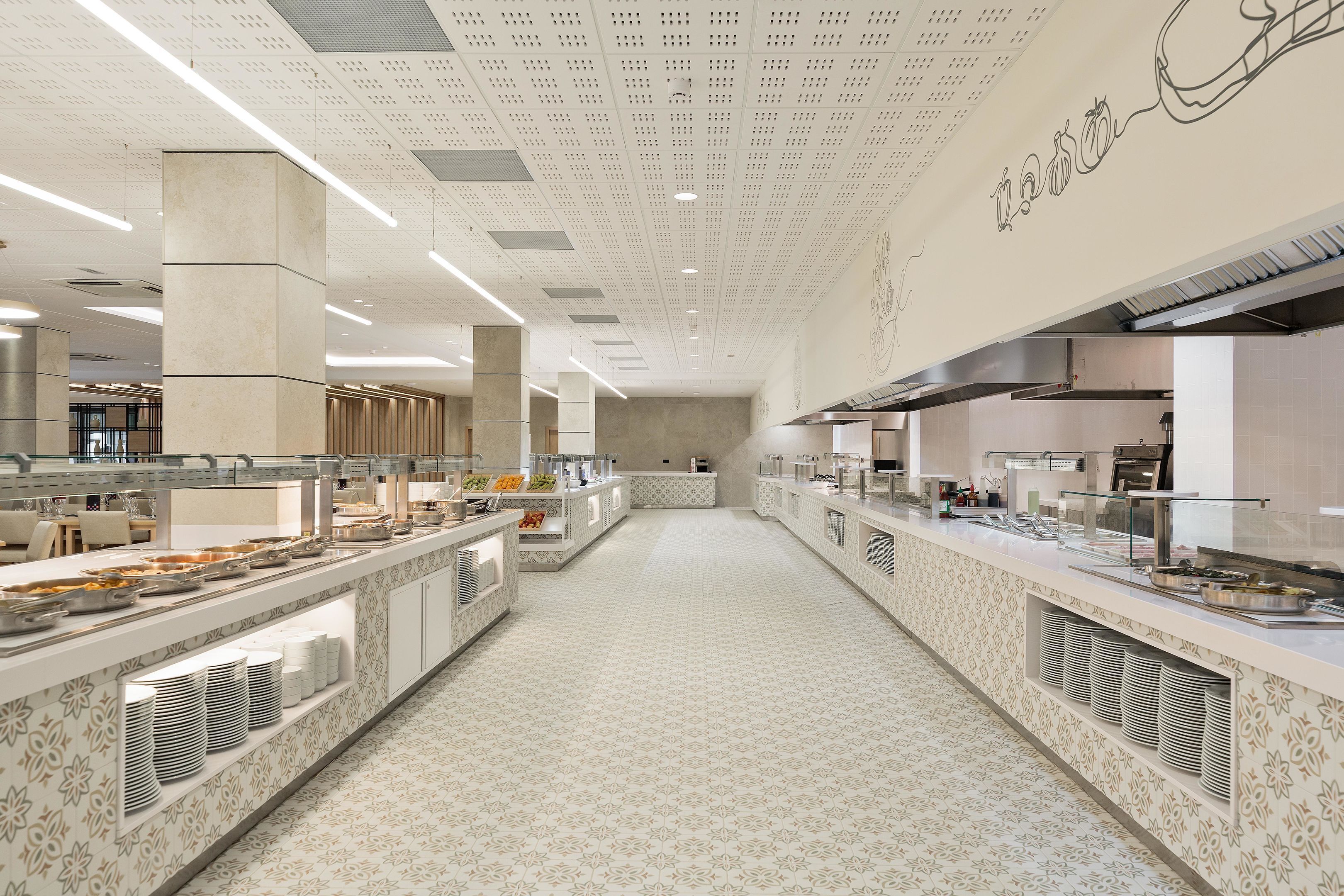 A spacious buffet area with multiple serving stations, a patterned floor, and a high ceiling with perforated panels.