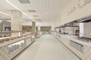 Un vaste espace buffet doté de plusieurs points de service, d’un sol à motifs et d’un plafond haut orné de panneaux perforés.