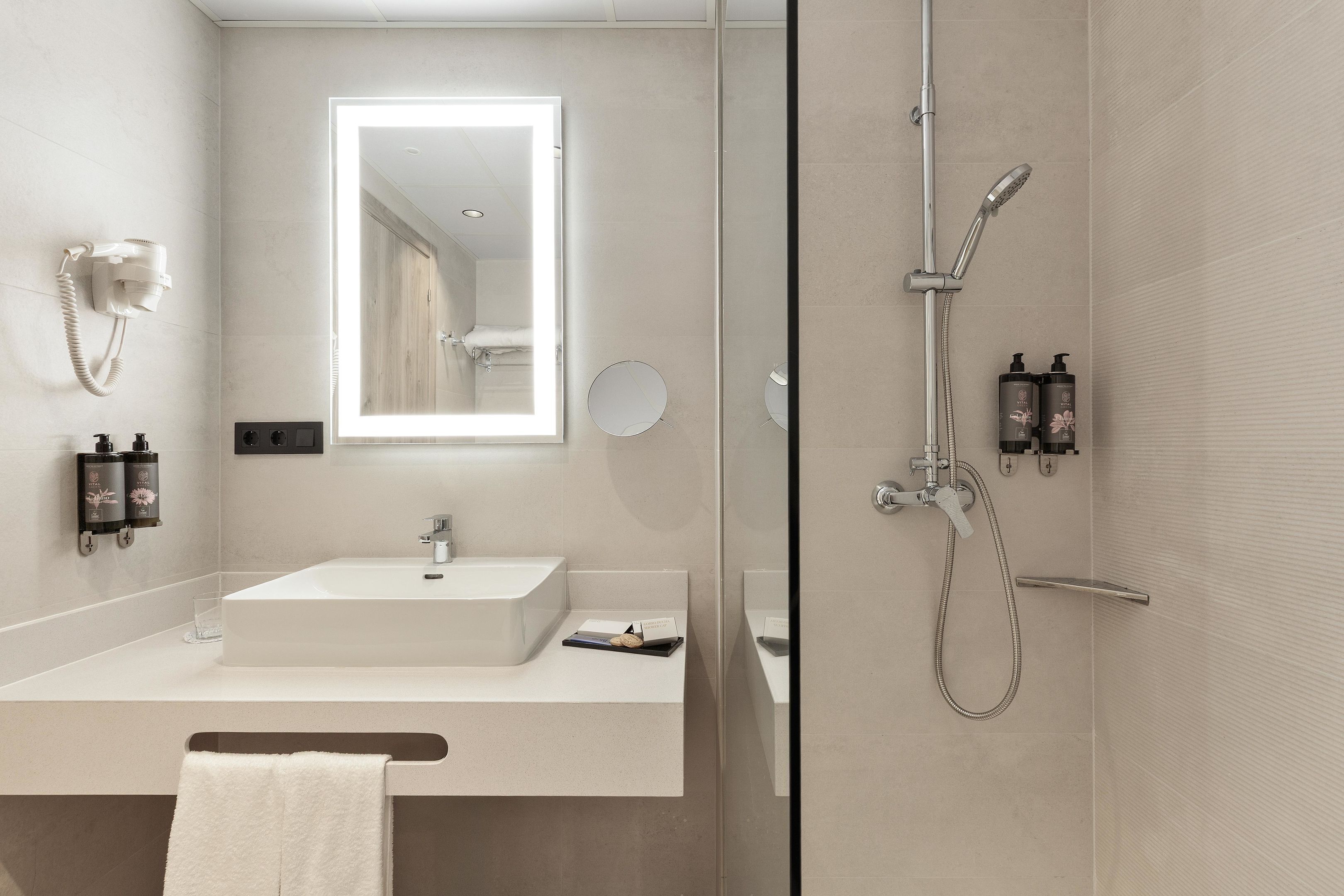 A modern bathroom with a large mirror, a sink, a handheld showerhead, and a towel rack.