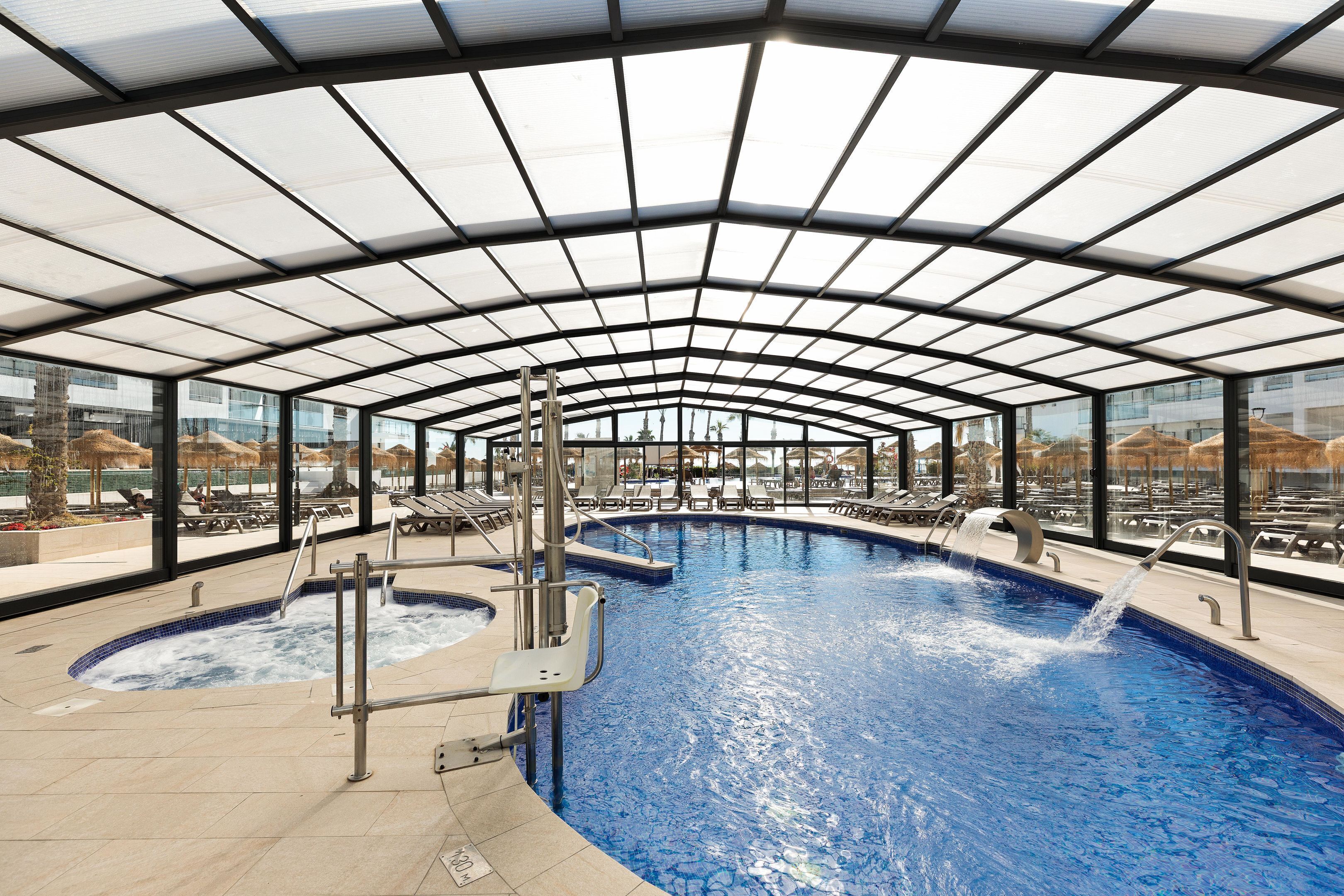 An indoor swimming pool with a glass ceiling, multiple lanes, and a jacuzzi area.