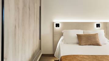 A neatly made bed with white linens and a brown accent pillow, a wooden wardrobe, and a wall-mounted light fixture.