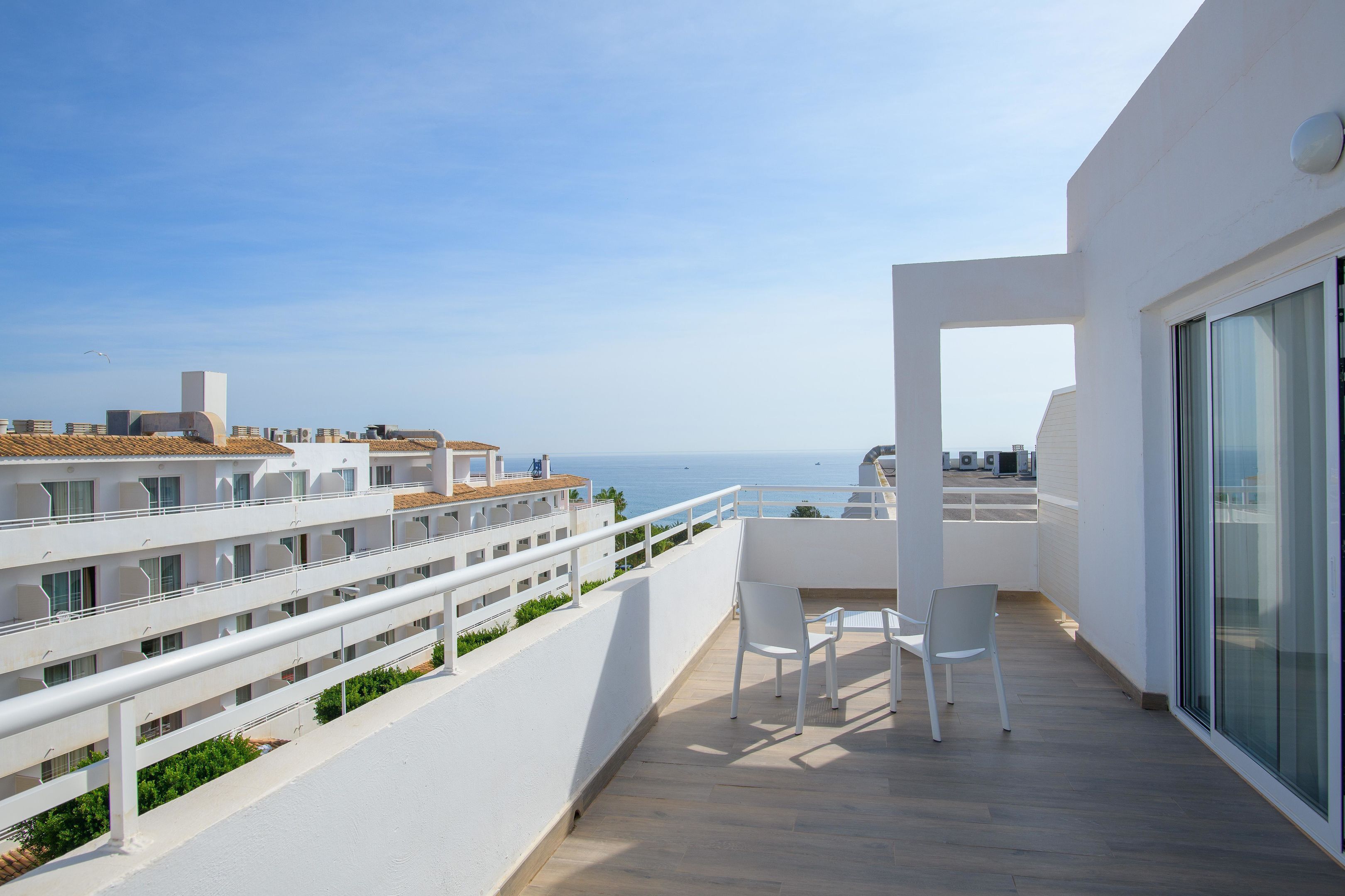 Un balcon avec vue sur la mer, des balustrades blanches et une table avec des chaises.