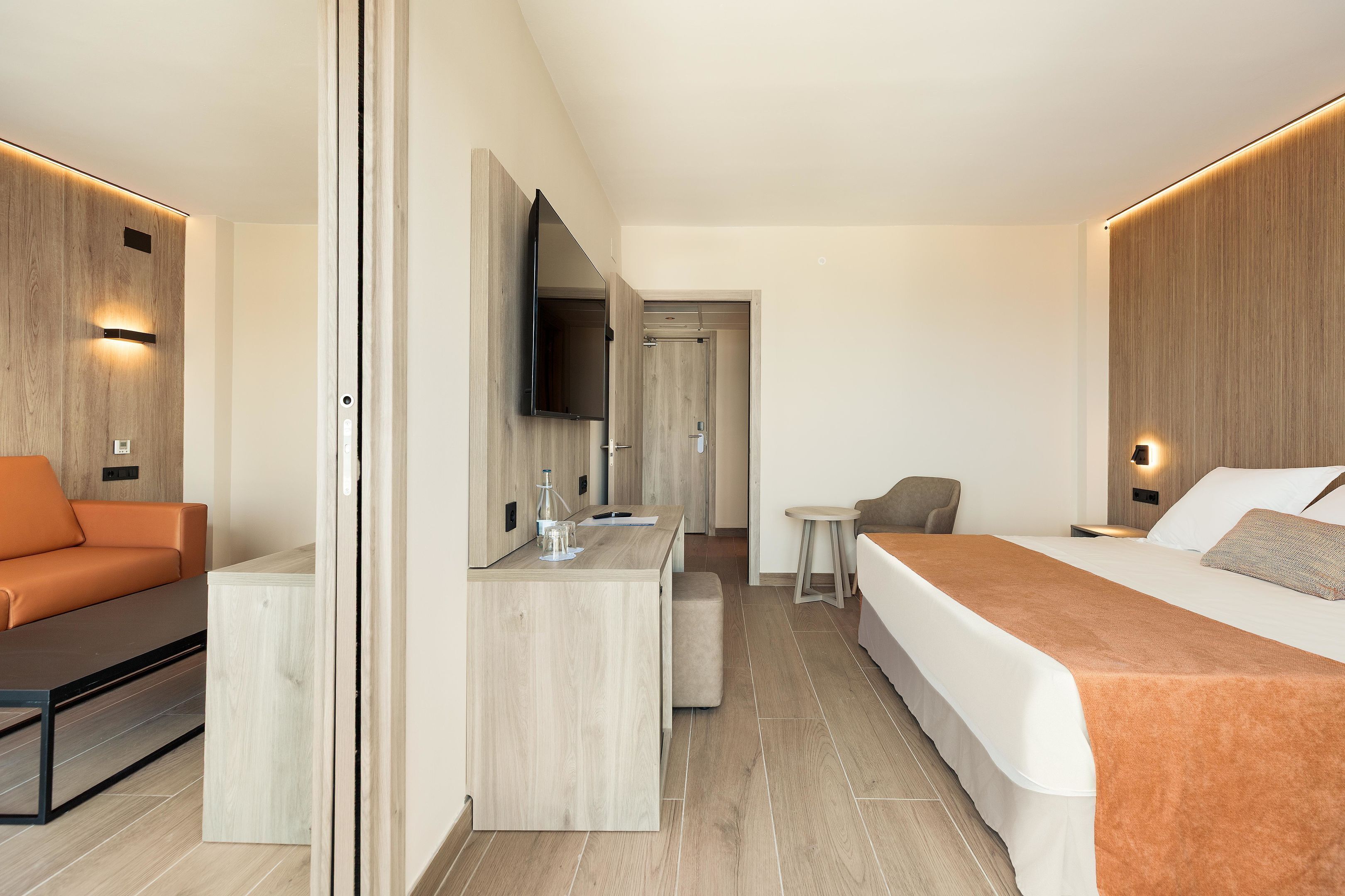 A modern hotel room with a bed, a sofa, a desk, and a TV.