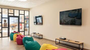 A modern interior with bean bags, a painting, and a television on the wall.