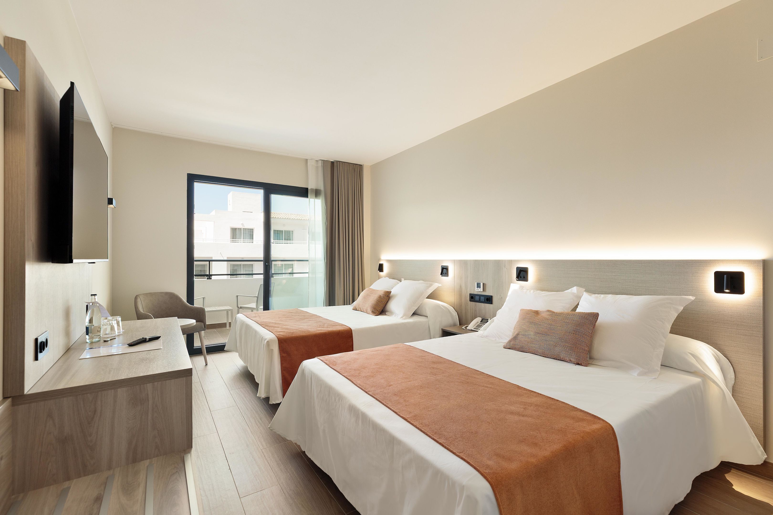 A hotel room with two beds, a desk, a chair, a TV, and a balcony with a view.