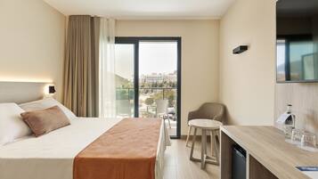 A hotel room with a bed, a small dining area, a chair, a TV, and a view of the city.