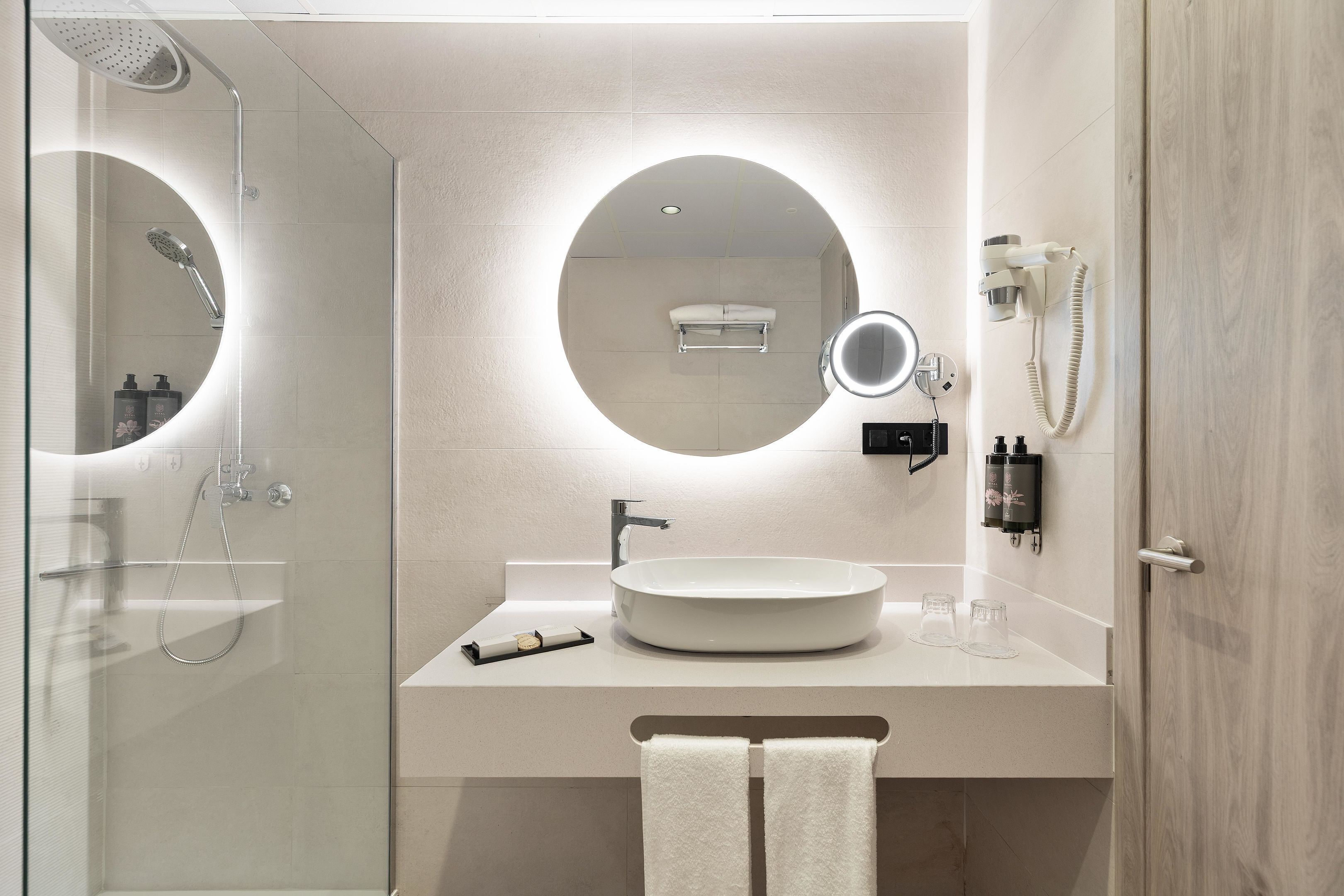 A modern bathroom with a glass-enclosed shower, a round mirror, a sink, and a towel rack.