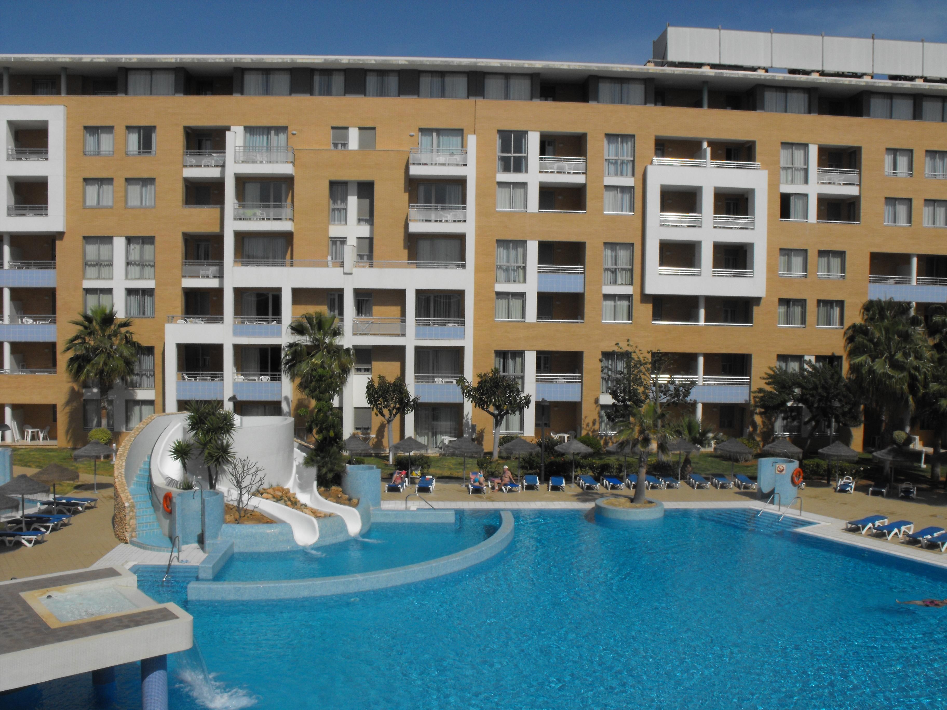 Een hotel met een zwembad, inclusief een waterglijbaan en ligbedden.
