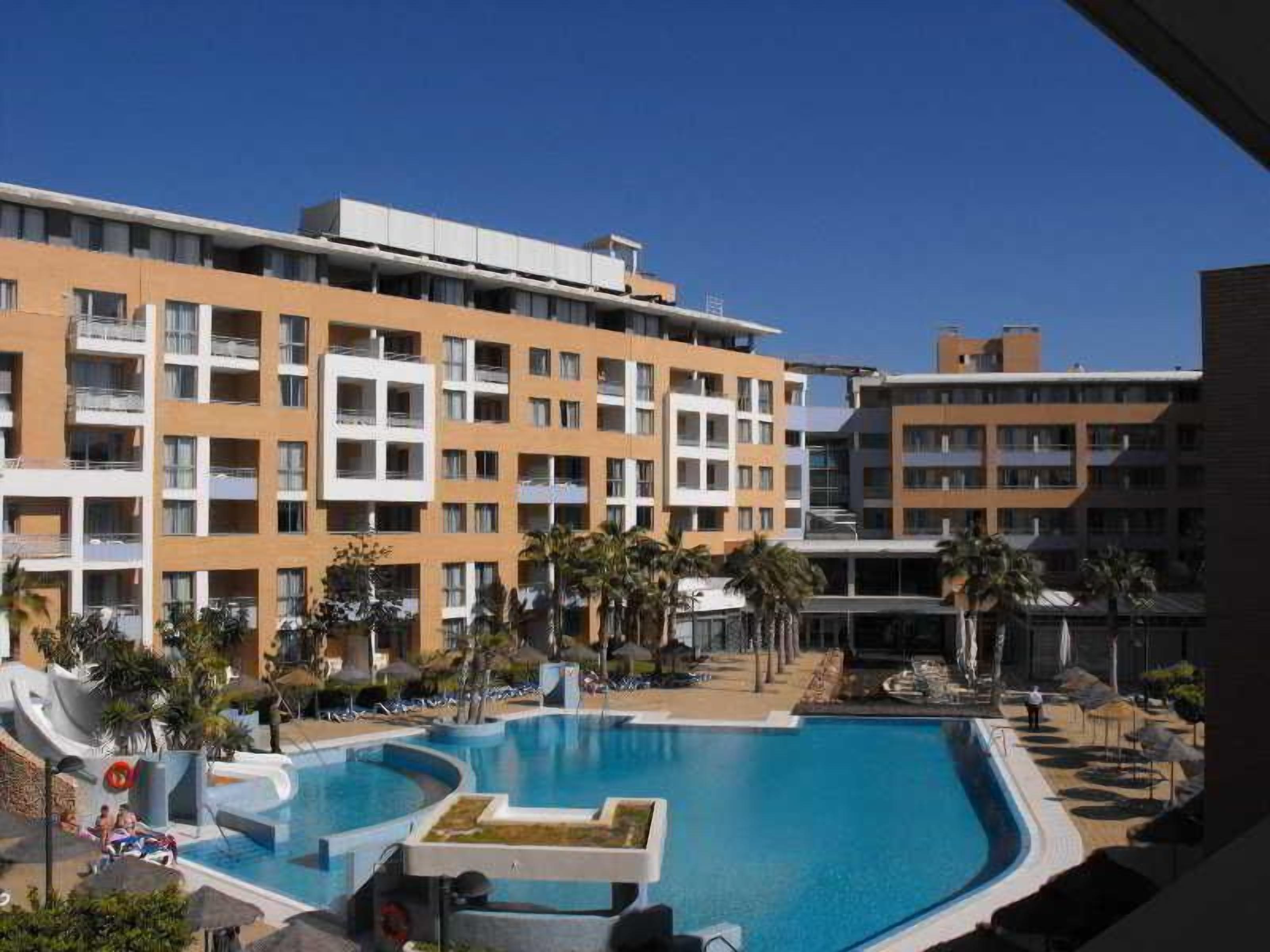 Un hotel con piscina rodeada de palmeras y sillas de descanso.