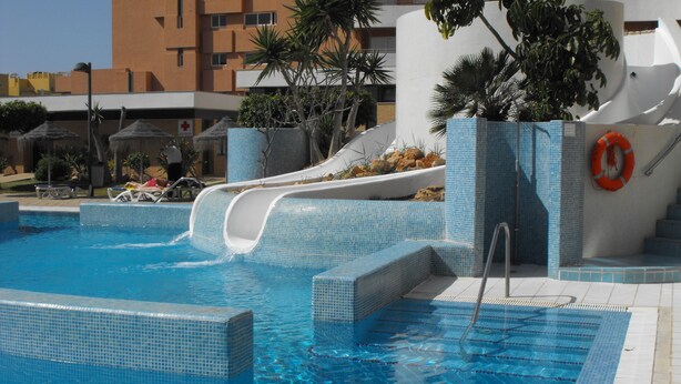 A swimming pool with a water slide, lounge chairs, and a lifebuoy. - Neptuno (Roquetas de Mar)