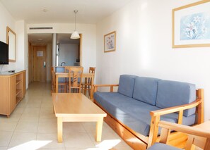 A living room with a sofa, a wooden table, a TV, and a kitchen area in the background. - Neptuno (Roquetas de Mar)