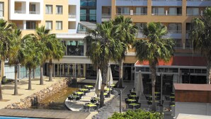A hotel with multiple floors, outdoor seating area with umbrellas, and palm trees. - Neptuno (Roquetas de Mar)