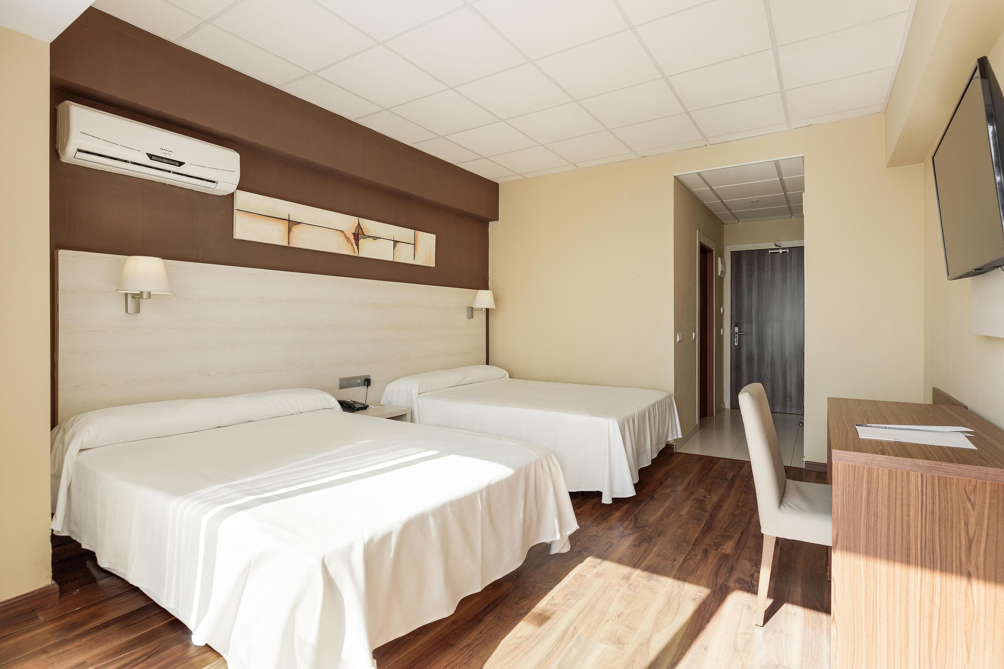 A hotel room with two beds, a desk, a chair, an air conditioning unit, and a television on the wall.