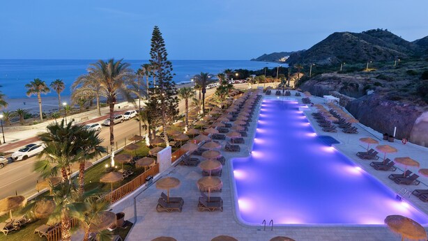 A poolside area with lounge chairs and umbrellas, a swimming pool, and a view of the beach and ocean. - Hotel Best Indalo (Mojacar)