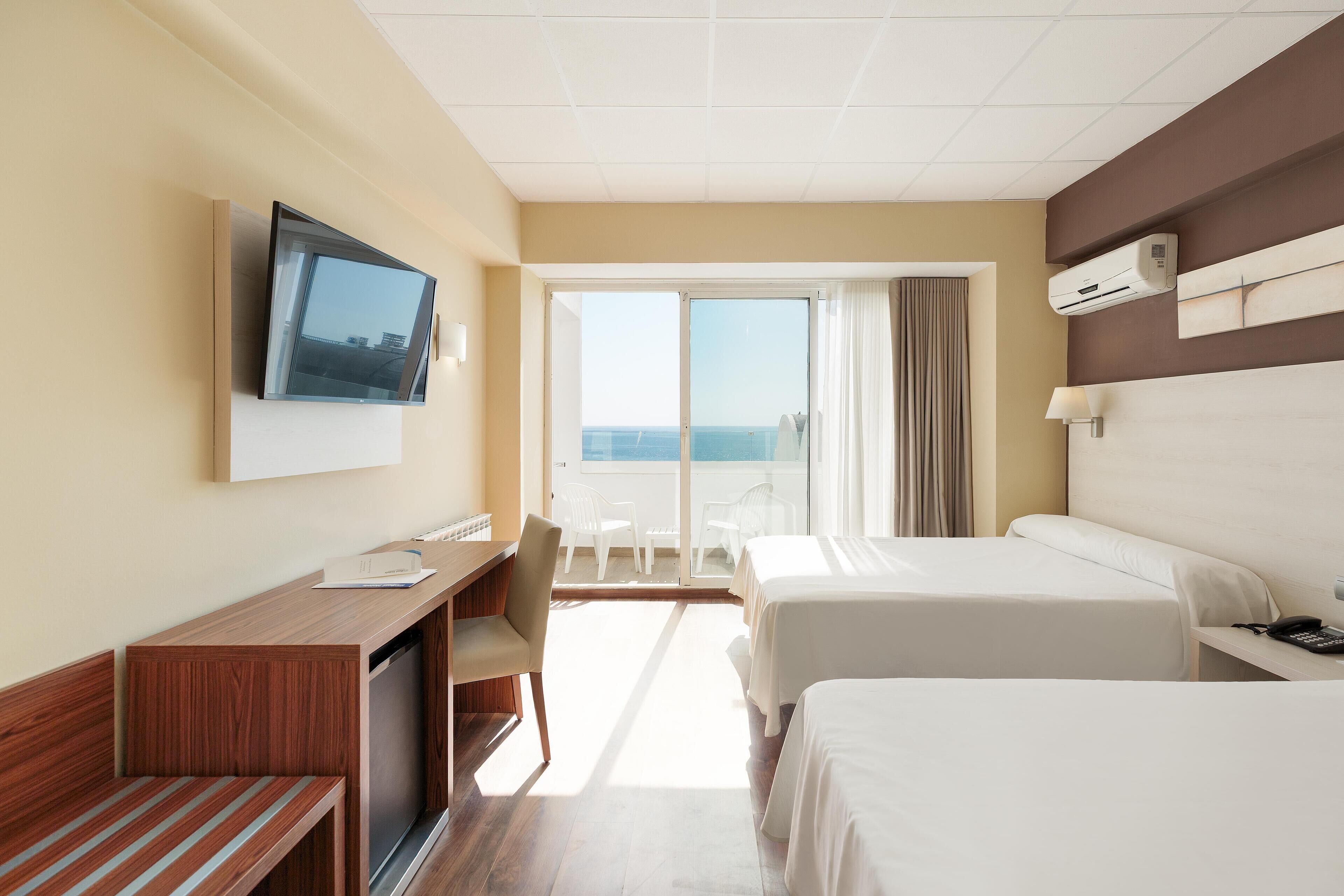 Une chambre d’hôtel avec deux lits, un bureau, une télévision et un balcon donnant sur la mer.