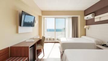 Une chambre d’hôtel avec deux lits, un bureau, une télévision et un balcon donnant sur la mer.