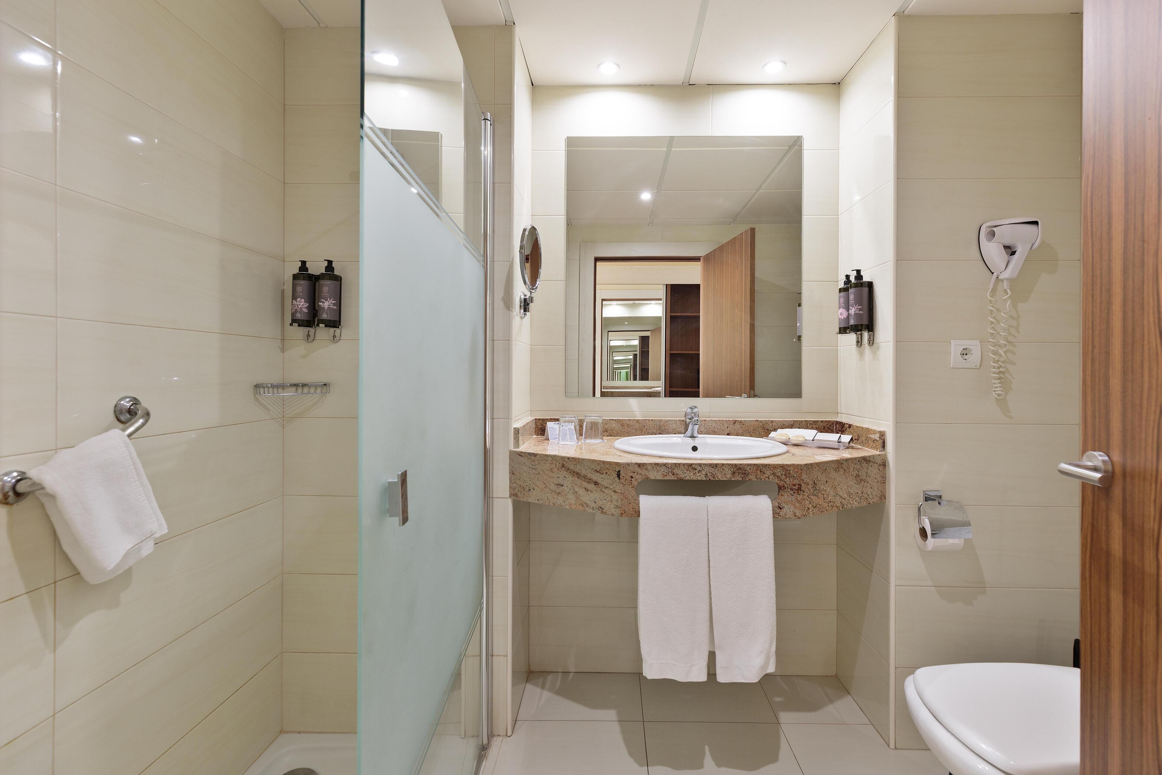 Un baño moderno con cabina de ducha de vidrio, lavamanos con encimera de mármol y inodoro.