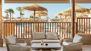 A balcony with wicker furniture, a table, and a view of a pool area with umbrellas and lounge chairs. - Hotel Best Indalo (Mojacar)