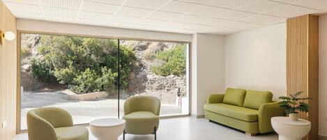A modern waiting area with a large window, two green armchairs, a white coffee table, and a green sofa.