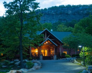 A lodge with a prominent front porch, a stone staircase leading up to the entrance, and a view of a rocky cliff in the background. - Minnewaska Lodge (Gardiner)