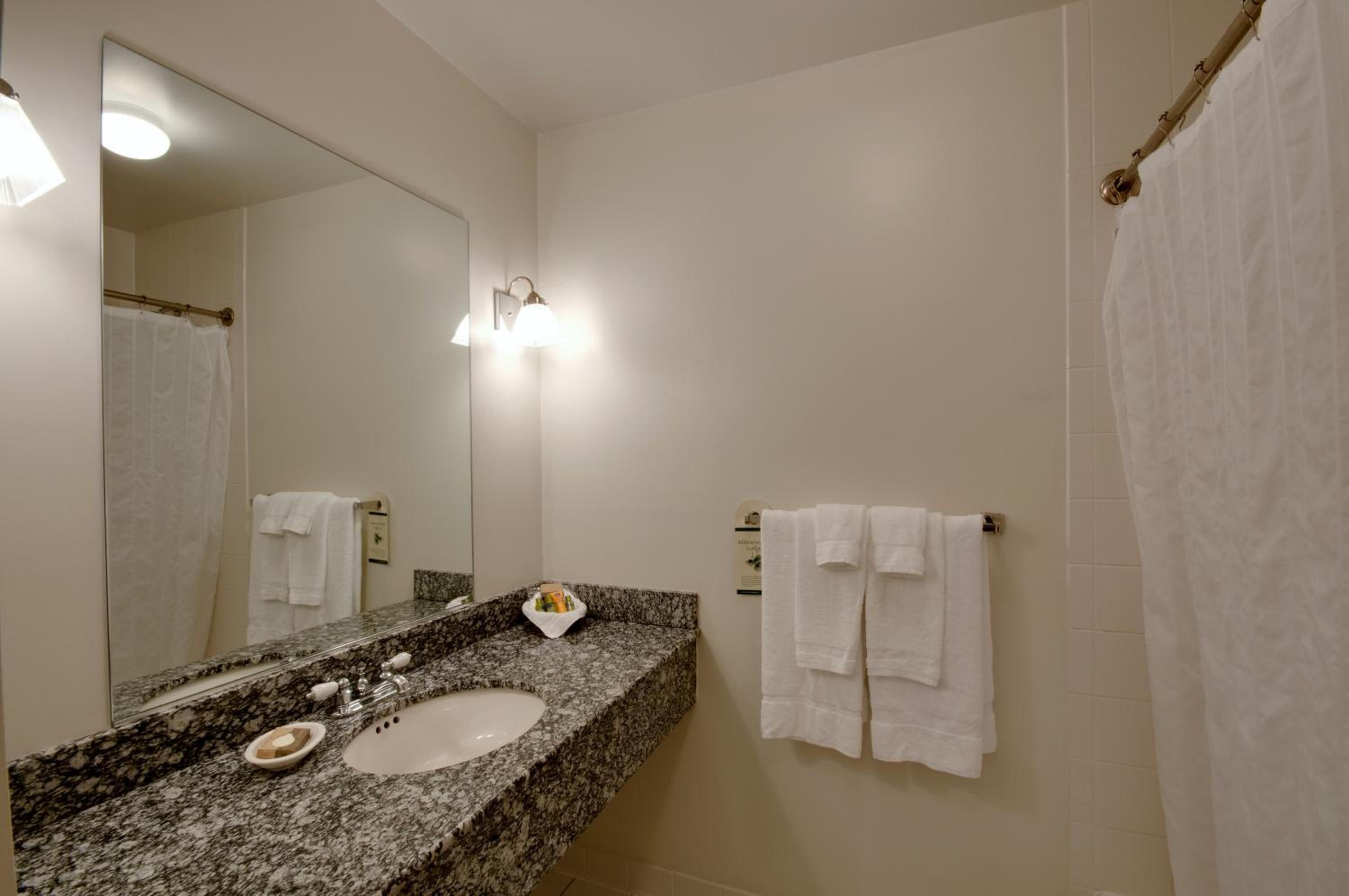 Baño con lavamanos de encimera de granito, espejo, toallero con varias toallas y cortina de ducha.