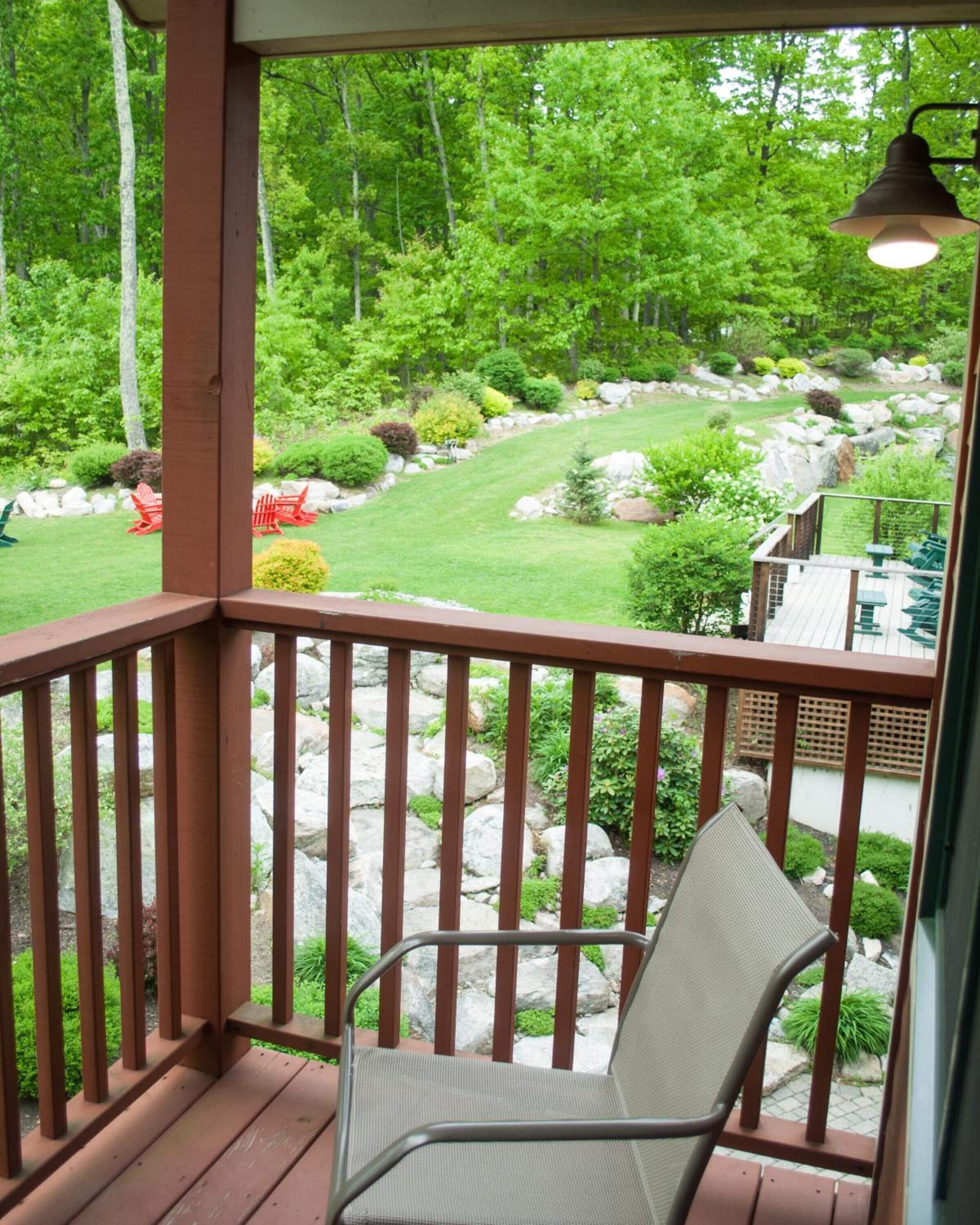 A wooden deck with a chair, overlooking a landscaped garden with rocks, bushes, and trees.
