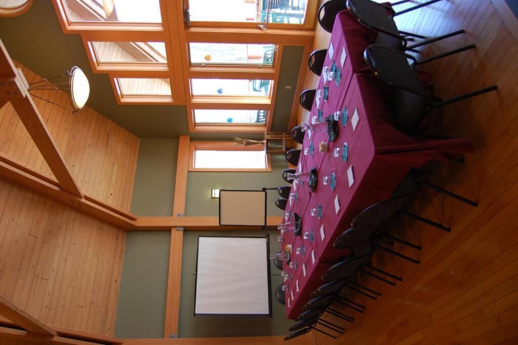 Uma sala de conferências com uma mesa comprida, cadeiras, uma tela de projetor e claraboias.