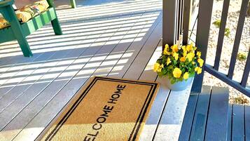 Una terraza de madera con un felpudo, un banco y una planta en maceta.