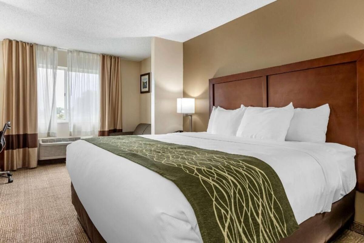 Une chambre d’hôtel avec un grand lit, un bureau, une chaise, une lampe et une fenêtre avec des rideaux.