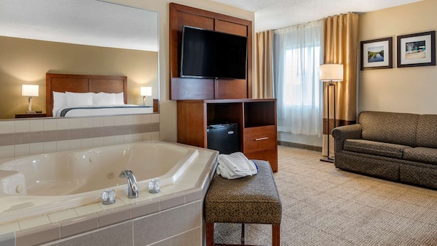 A hotel room with a large bathtub, a sofa, a TV mounted on a wooden cabinet, and a small table with towels.