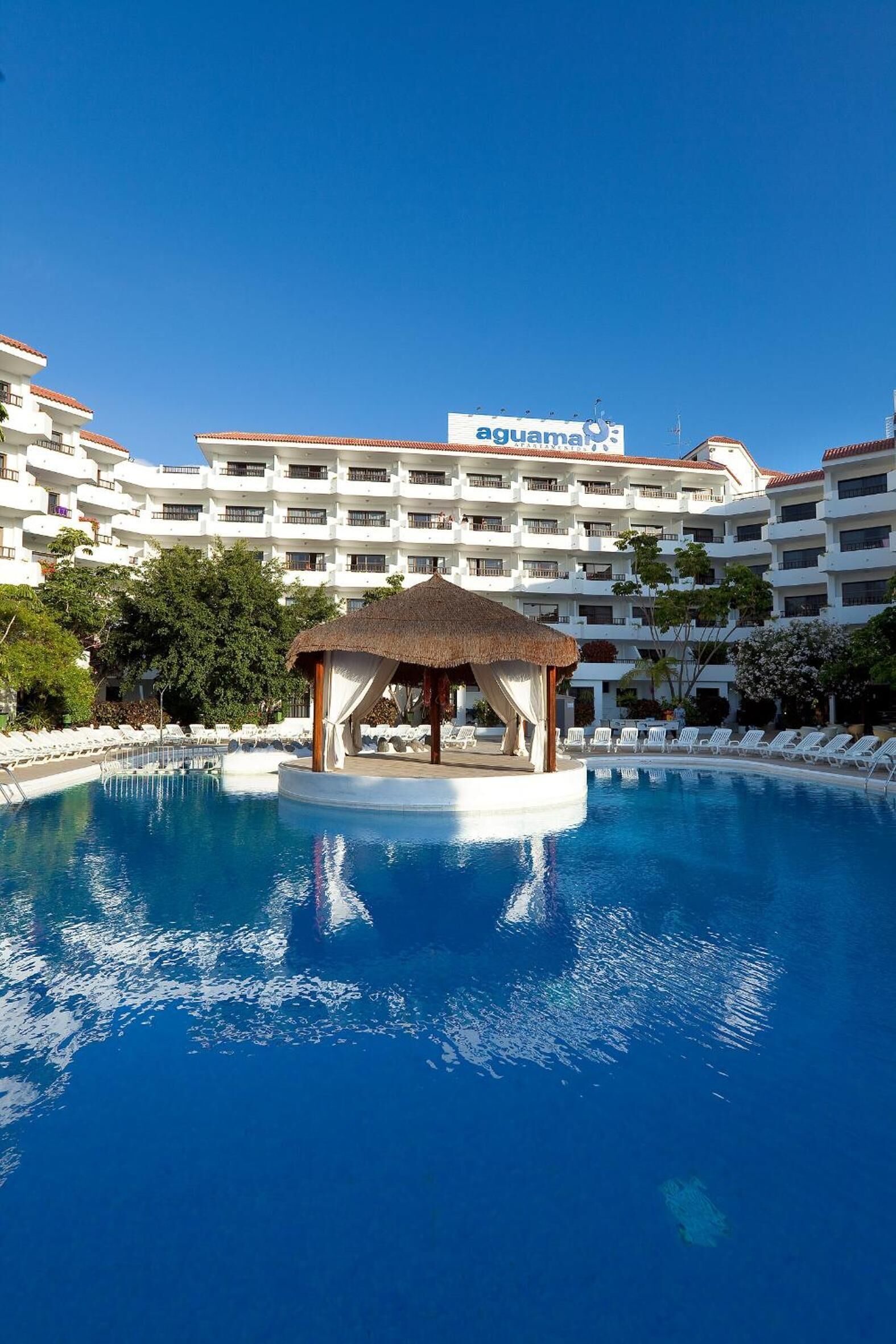 A hotel pool with a gazebo, white buildings, and a clear blue sky.