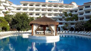 A hotel pool with a gazebo, white buildings, and a clear blue sky.
