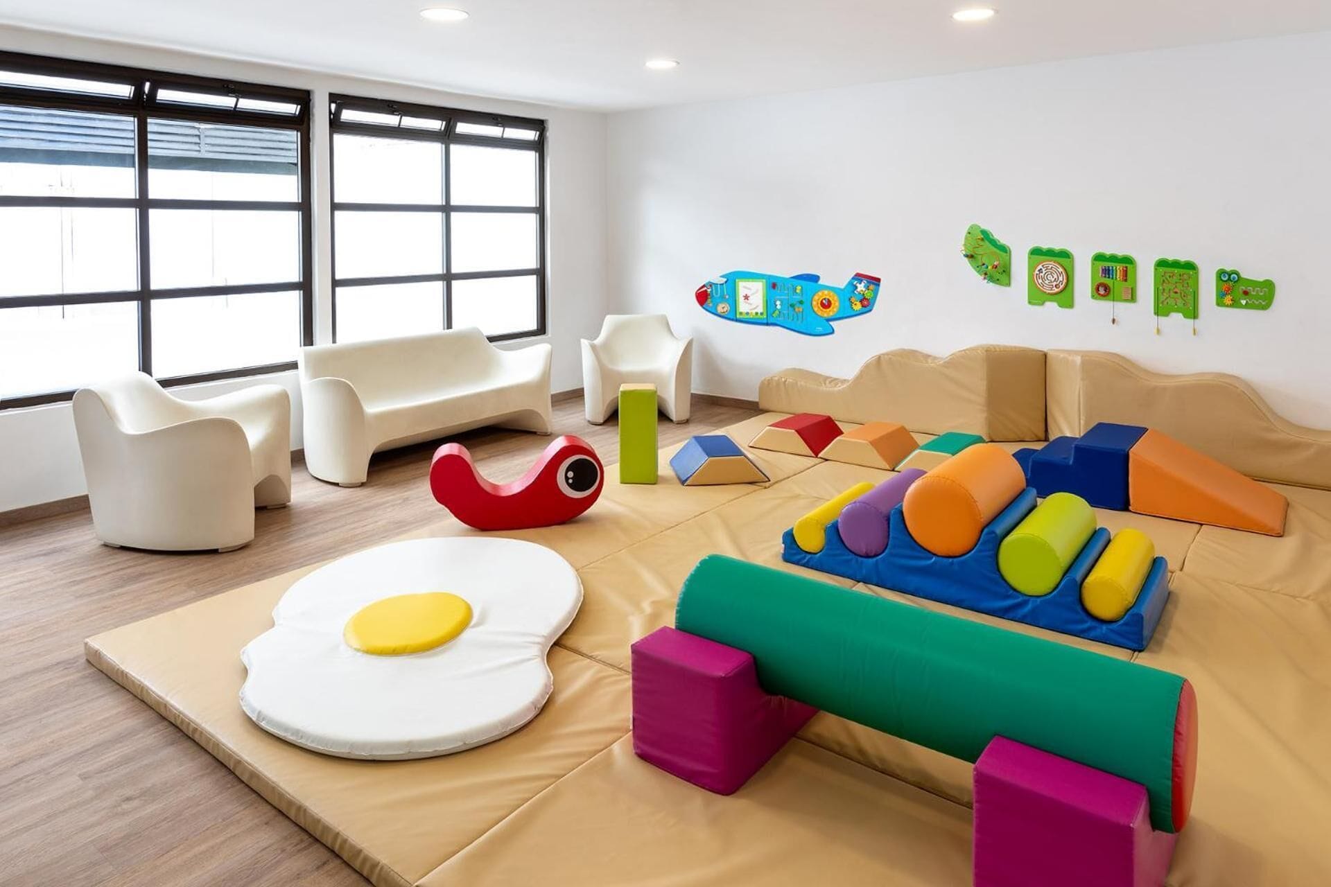 Une salle de jeux moderne avec une grande fenêtre, des canapés blancs et des structures de jeu colorées.