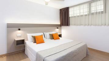 A modern hotel room with a large bed, two bedside tables, a ceiling fan, and a window with curtains.