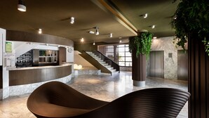 Un hall d’entrée moderne avec un espace salon aux lignes courbes, un comptoir d’accueil et un escalier menant à un niveau supérieur.