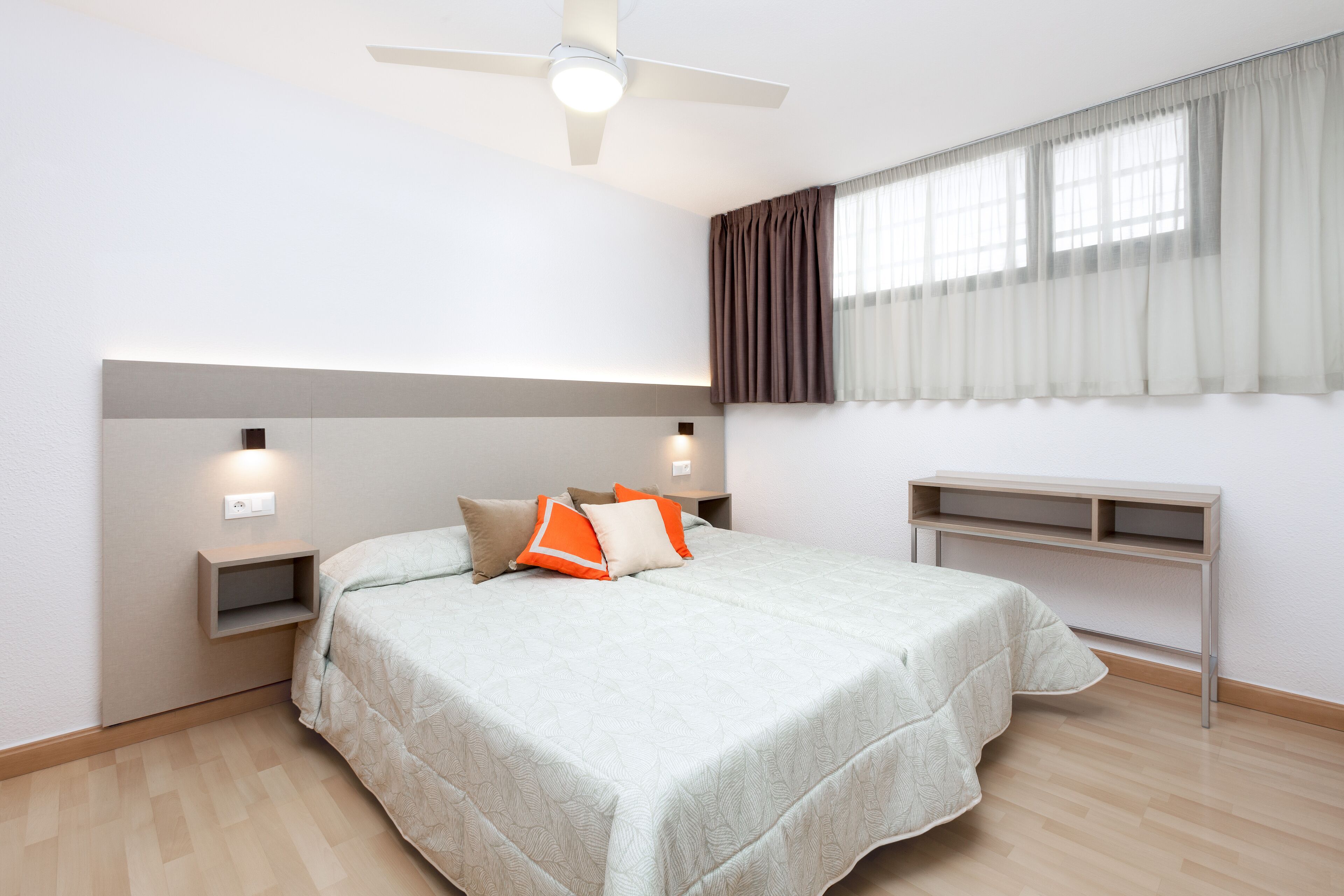 Una camera da letto con un letto, comodini, una scrivania, una ventola a soffitto e una finestra con tende.