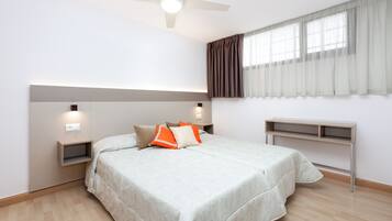 Una camera da letto con un letto, comodini, una scrivania, una ventola a soffitto e una finestra con tende.