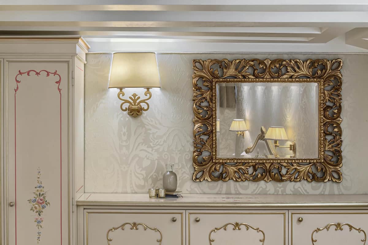 A wall with a decorative mirror, a wall sconce, and a cabinet with drawers.