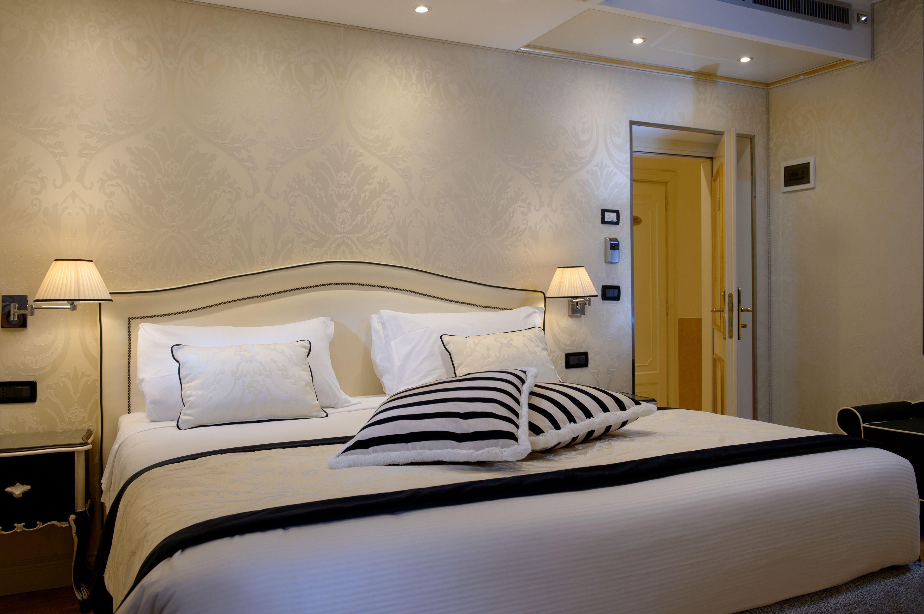 A neatly made bed with white and striped pillows, a black headboard, and two bedside lamps.